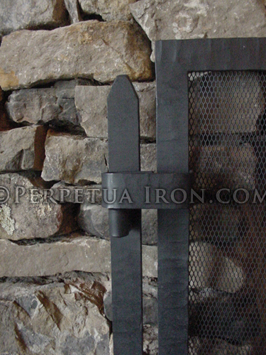 Close up detail of the hinges of an unembellished fireplace screen with textured steel frame in front of rustic fireplace mantel hand made in St Louis by Perpetua Iron.