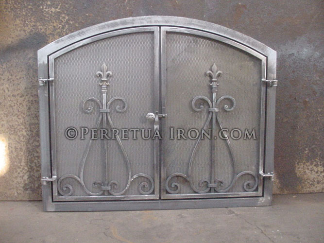 Wrought iron fireplace screen or fire door with arched top and fleur de lis pattern centered in each door.