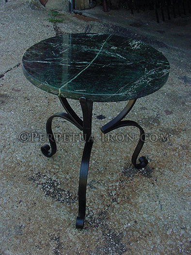 forged and bent table frame with round marble top sitting on concrete patio