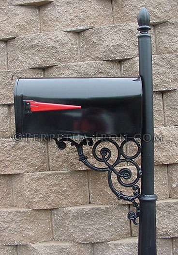 Black mailbox in front of a retaining wall, plain post with decorative bracket.