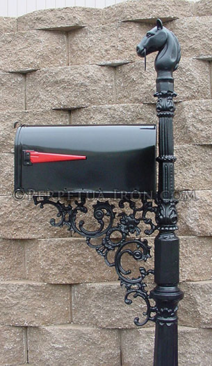 Fancy mailbox post in fron tof a retaining wall with extremely ornate support bracket. You can see a horse head on top of the post.