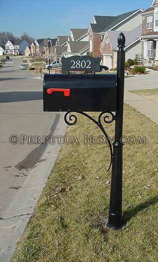Side view of a black mailbox and heavy iron post in a suburban neighborhood.