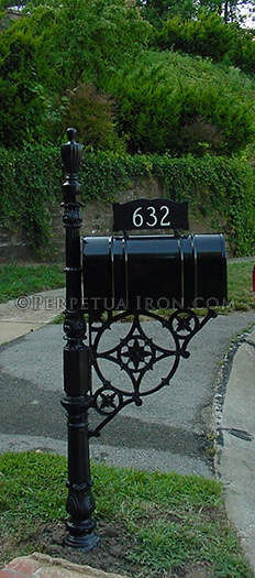 An installed mailbox with the star-in-circle bracket and heavy, ornate iron post. House number is mounted to top of mailbox itself.