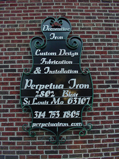 Black and white iron sign mounted to a brick wall is made from heavy weight iron with scrolls and steel letters.